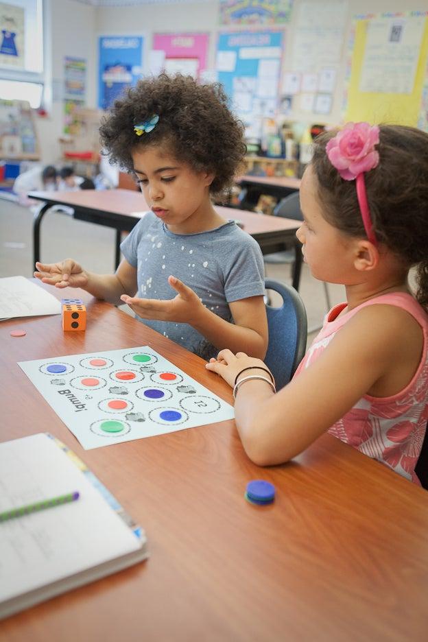 Two young students sit at a desk in a classroom with a math project.