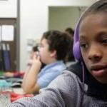 Two older elementary students in a computer lab talk and look at a monitor together