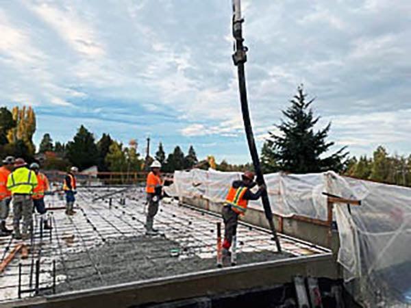 concrete is being pumped into framing with workers guiding the nozzle