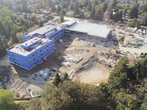 aerial view of a large L shaped building under construction with large holes dug in ground