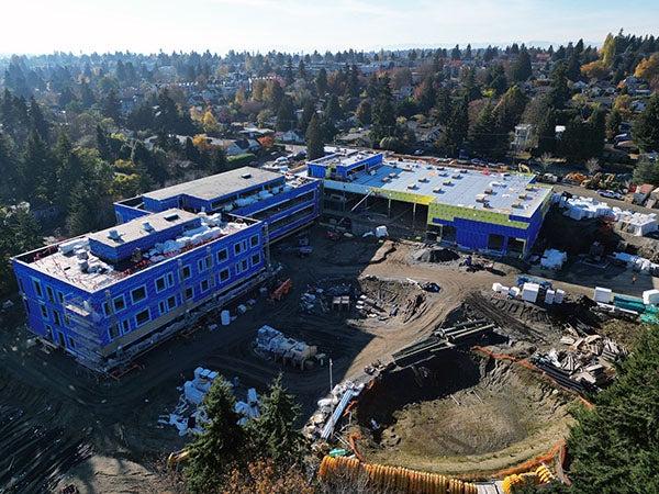 aerial photo of an L shaped building with a dirt area in front that includes a large hole