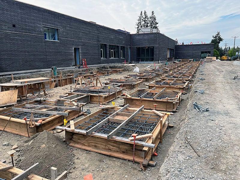 square concrete forms with rebar are in front of a brown brick building