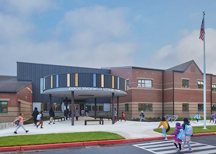 a two story brick building has a round canopy with a striped facade in fron covering a breezeway toward the entrance. a pave sidewalk and a walkway are in front. there are students walking toward the entrance.